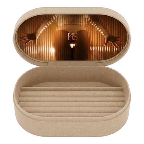 An open oval eyeglasses case in a warm beige fabric, featuring a printed design on the inside lid of a figure in a red and gold corset with outstretched arms under a curtain, with a small 'KS' monogram at the top.