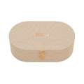 An oval-shaped beige textured cosmetic box with a small rose gold metal logo plaque on the lid and a matching vertical clasp, shown on a clean white background.