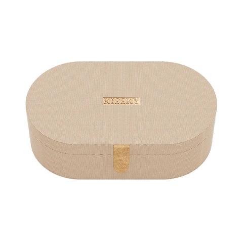 An oval-shaped beige textured cosmetic box with a small rose gold metal logo plaque on the lid and a matching vertical clasp, shown on a clean white background.