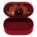 An open oval red eyeglasses case with a dark red velvet-lined interior, featuring a dramatic stage-like reflection on the inside lid with hands and a spotlight, and a small 'VS' monogram in the center.