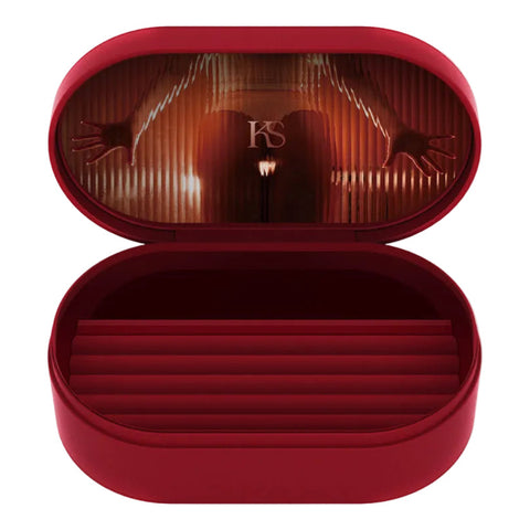An open oval red eyeglasses case with a dark red velvet-lined interior, featuring a dramatic stage-like reflection on the inside lid with hands and a spotlight, and a small 'VS' monogram in the center.