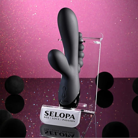 Black silicone product on a clear stand with 'SELOPA' branding against a pink glittery background.