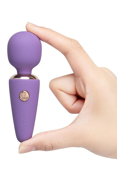 Purple handheld massager held by a hand on a white background