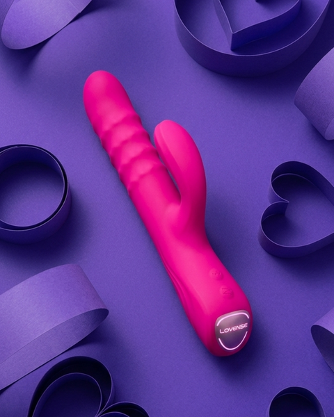 A bright pink personal massager with a cactus-like curved design, photographed on a purple background with decorative paper heart and loop props.