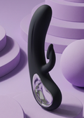 A black curved personal massager with a metallic silver inner ring, displayed on a purple studio pedestal.